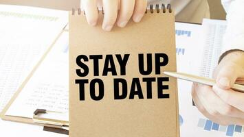 Text STAY UP TO DATE on brown paper notepad in businessman hands on the table with diagram. Business concept photo