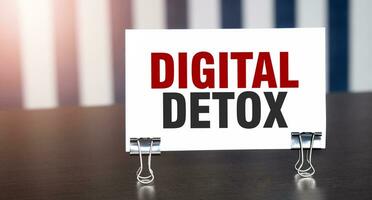 DIGITAL DETOX sign on paper on dark desk in sunlight. Blue and white background photo