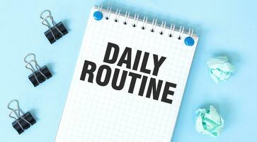 White notepad with text DAILY ROUTINe and office tools on the blue background photo