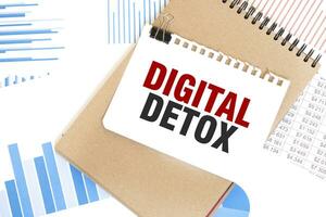 Text DIGITAL DETOX on white paper sheet and brown paper notepad on the table with diagram. Business concept photo