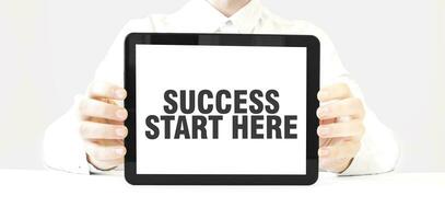 Text SUCCESS START HERE on tablet display in businessman hands on the white background. Business concept photo