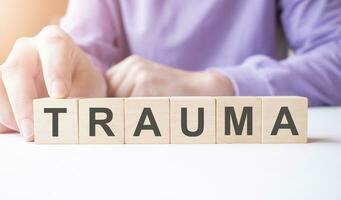 Businessman hand holding wooden cube block with TRAUMA business word on table background. photo