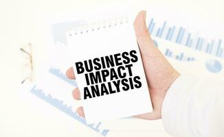 Businessman holding a white notepad with text BUSINESS IMPACT ANALYSIS, business concept photo