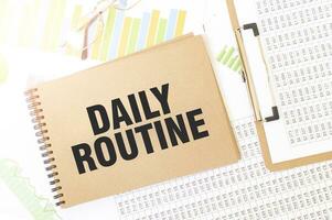 Business up graph on a sheet of craft colour Notepad with DAILY ROUTINE sign. Notepad on desk with financial documentation photo