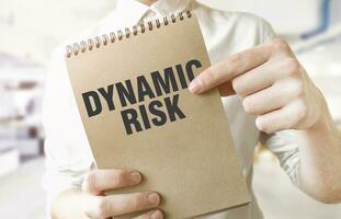 Text DYNAMIC RISK on brown paper notepad in businessman hands in office. Business concept photo