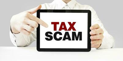 Text TAX SCAM on tablet display in businessman hands on the white background. Business concept photo