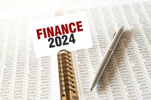 Text FINANCE 2024 on paper card, pen, financial documentation on table photo