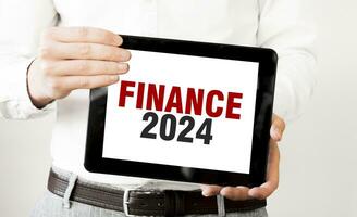 Text FINANCE 2024 on tablet display in businessman hands on the white background. Business concept photo