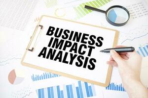 Text BUSINESS IMPACT ANALYSIS on white paper sheet and marker on businessman hand on the diagram. Business concept photo