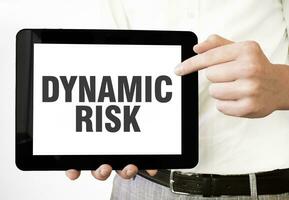 Text DYNAMIC RISK on tablet display in businessman hands on the white background. Business concept photo