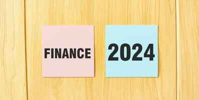 Inscription FINANCE 2024 on pink and blue square sticky sticker on wooden wall photo