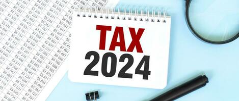 White notepad and magnifier on the financial documentation. Text TAX 2024. Business concept photo