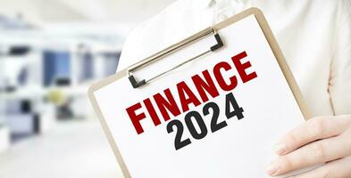 Text FINANCE 2024 on white paper plate in businessman hands in office. Business concept photo