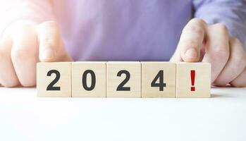 Businessman hand holding wooden cube block with 2024 business word on table background. photo