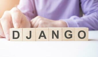 Businessman hand holding wooden cube block with DJANGO business word on table background. photo