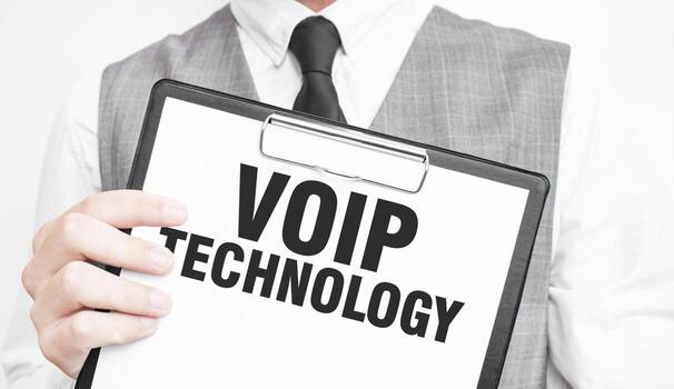 VOIP TECHNOLOGY inscription on a notebook in the hands of a businessman on a gray background, a man points with a finger to the text photo