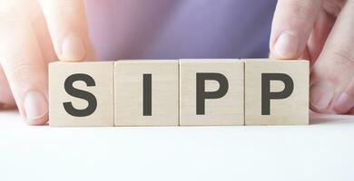 Businessman hand holding wooden cube block with SIPP business word on table background. photo