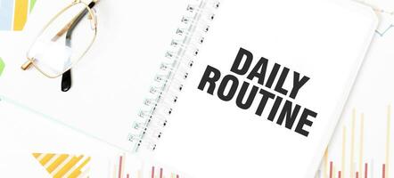 Text DAILY ROUTINe on white notepad, glasses, graphs and diagrams. photo