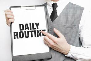 DAILY ROUTINe inscription on a notebook in the hands of a businessman on a gray background, a man points with a finger to the text photo