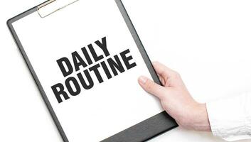 A businessman holds a folder with paper sheet with the text DAILY ROUTINe. Business concept. photo