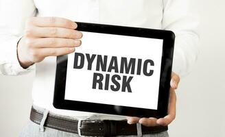 Text DYNAMIC RISK on tablet display in businessman hands on the white background. Business concept photo