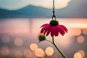 a pink flower hanging from a chain by a lake. AI-Generated photo