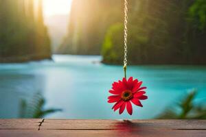 a red flower hanging from a chain by a lake. AI-Generated photo