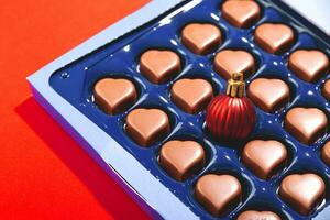 Creative Christmas concept with Christmas ball in box of heart shaped chocolates. photo