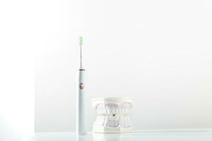 Electronic toothbrush next to jaw model with teeth on light background of bathroom. Minimal background with copy space. photo