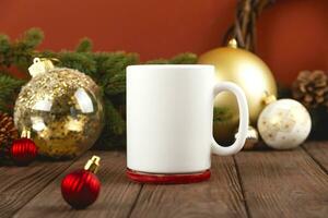 Christmas mock up of white mug on wooden table with festive decorations. Golden Christmas balls against red wall. photo