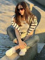 a woman sitting on a ledge wearing sunglasses and a striped shirt photo