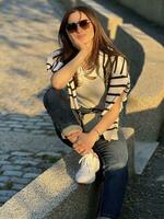 Photo of a woman sitting on a stone bench wearing sunglasses