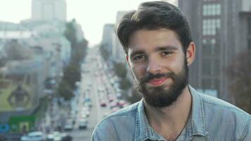 Young bearded man smiling to the camera with city on background video