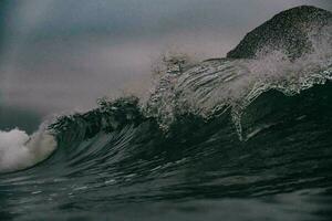 a wave breaking on the ocean with dark blurry sky in background photo