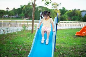 linda niña asiática sonríe jugar en la escuela o en el jardín de infantes o en el patio de recreo. Actividad de verano saludable para niños. niña asiática escalando al aire libre en el patio de recreo. niño jugando en el patio de recreo al aire libre. foto