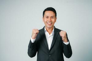 asiático empresario en traje con contento expresión y levanta su mano en pie estudio aislado en gris fondo, joven negocio hombre es gerente o ejecutivo sonriente y confidente es positivo éxito. foto