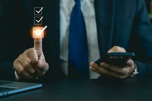 Businessman using finger to tick correct sign mark in virtual checkbox screen for quality document control checklist and business approve project. Businessman Take an assessment, questionnaire. photo