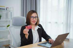 mujer de negocios participación crédito tarjeta y utilizando ordenador portátil computadora a compras en línea. mujer de negocios trabajando a hogar. en línea compras, comercio electrónico, Internet bancario, gasto dinero, compras desde en cualquier lugar. foto