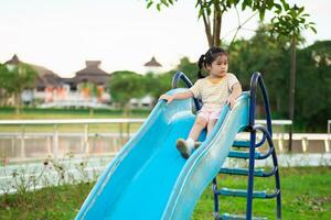 Cute asian girl smile play on school or kindergarten yard or playground. Healthy summer activity for children. Little asian girl climbing outdoors at playground. Child playing on outdoor playground. photo