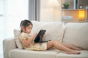 Asian child girl using pen and touch drawing on tablet display screen. Baby smiling funny time to use tablet. Too much screen time. Cute girl watching videos while tv, Internet addiction concept. photo