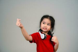 Cheerful happy asian children girl with black hair listening to music songs in headphones on a gray background. Portrait cute girl waring red shirt and looking at camera studio lighting. photo