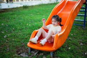 Cute asian girl smile play on school or kindergarten yard or playground. Healthy summer activity for children. Little asian girl climbing outdoors at playground. Child playing on outdoor playground. photo