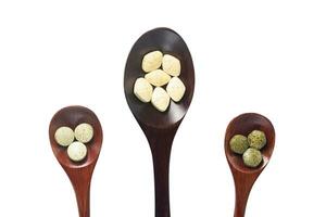 multivitaminas, multimineral, y fitonutrientes son presionado tabletas como nutricional suplementos metido en un grande de madera cuchara y pequeño de madera cuchara con aislado en blanco antecedentes. foto