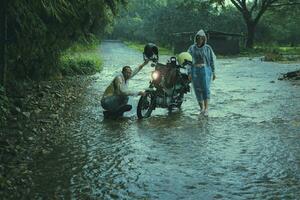 couples of asian biker wearing plastic rain clothes  maintenance small enduro motorcycle in shallow creek among rain falling photo