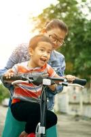 asian boy try to riding home bicycle with mother photo