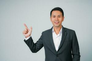 Asian businessman in suit with happy expression and raises his finger standing studio isolated on gray background, young business man is manager or executive smiling and confident is positive success. photo