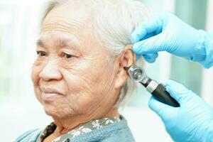 Otolaryngologist or ENT physician doctor examining senior patient ear with otoscope, hearing loss problem. photo