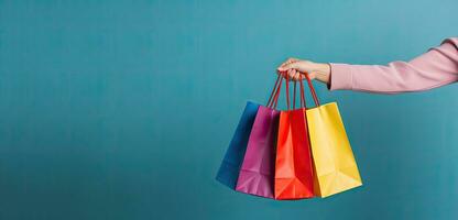 Colorful shopping bags in female hand on blue background. Copy space, Female hand holding many colorful shopping bags on blue background, AI Generated photo
