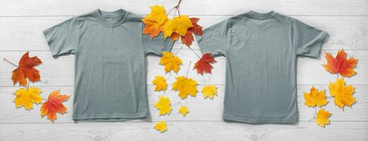 Front and back views on boys t-shirts on white wooden desk background with autumn lievs. Mockup for design closeup photo