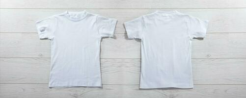 Front and back views on boys t-shirts on white wooden desk background. Mockup for design closeup photo